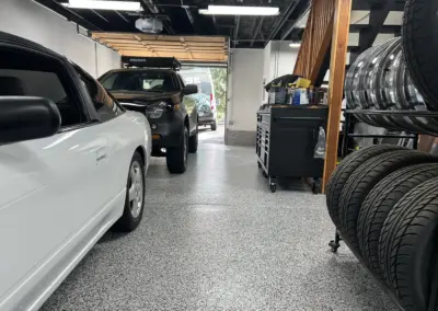 Garage floor with a light gray flake coating next to parked cars and a tire rack