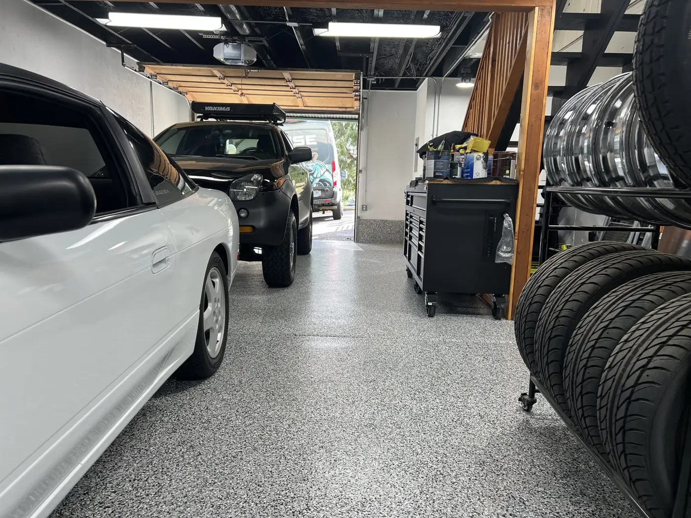 Garage floor with a light gray flake coating next to parked cars and a tire rack